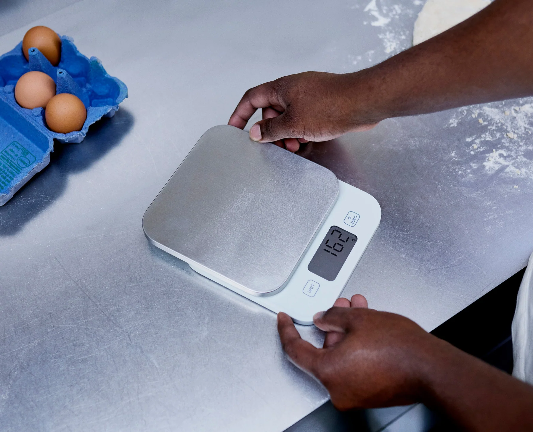 A digital kitchen scale on a countertop with a lightweight mixing bowl and a folded towel ready for weighing a kitten