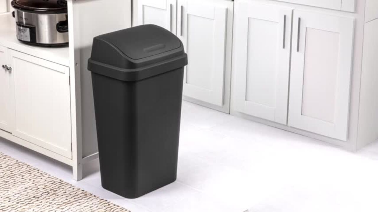 A small kitten sitting on a kitchen floor near closed cabinets and a lidded trash can in a tidy, kitten-safe setup