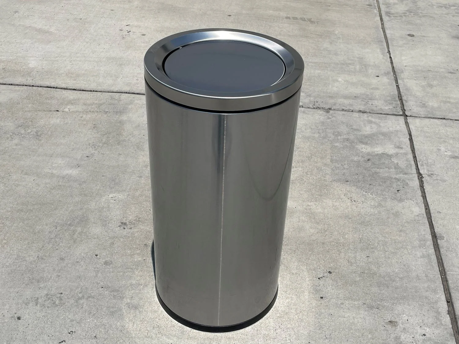 A stainless steel lidded kitchen trash can closed beside a cabinet on a clean kitchen floor